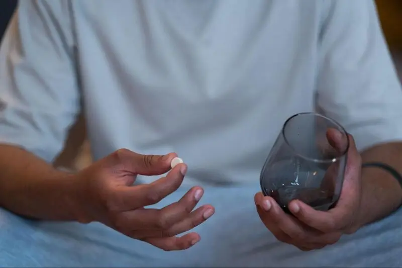a man holding a pill in one hand and a glass in other