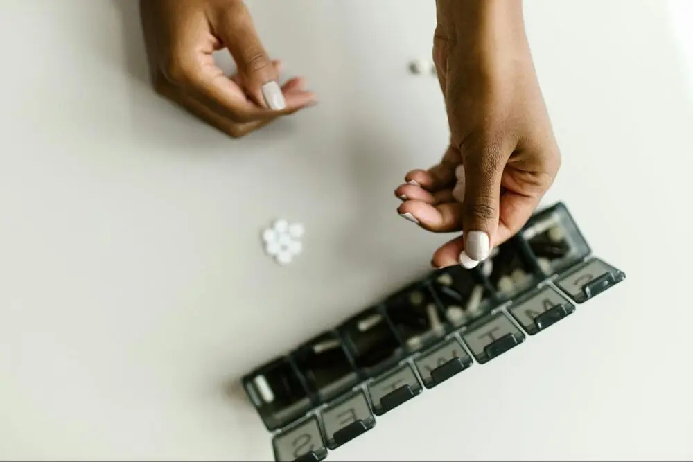 Person organizing daily medication in a weekly pill organizer