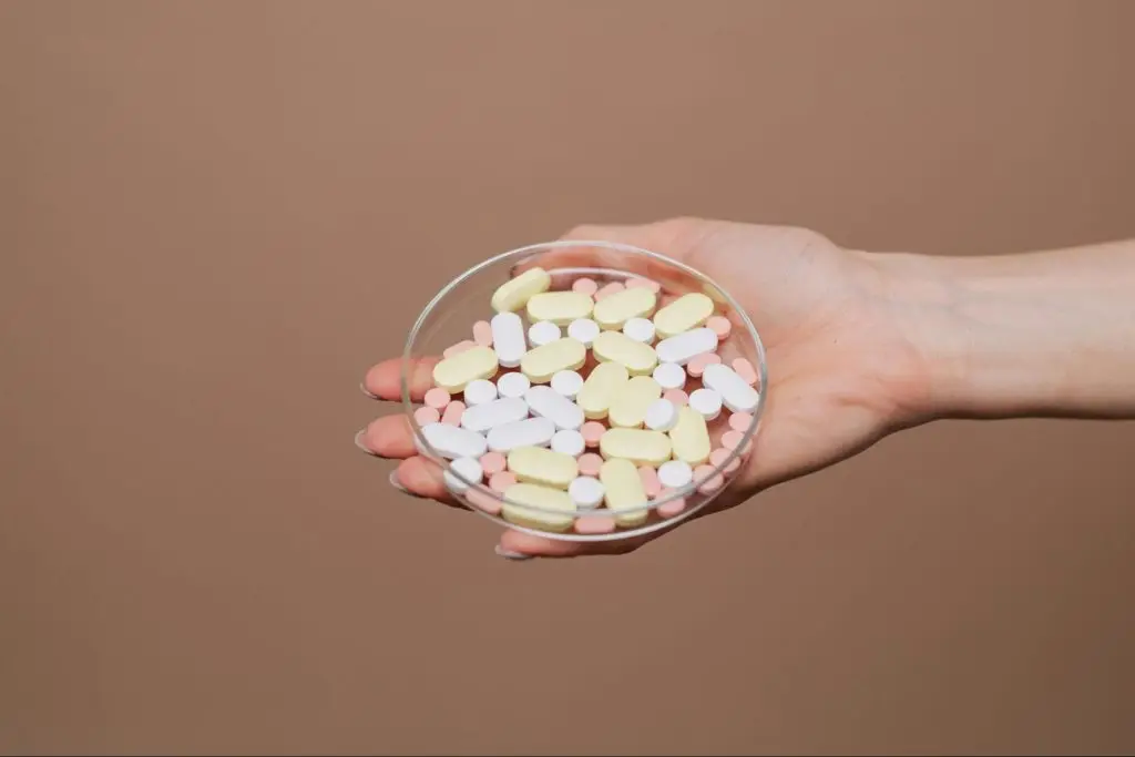 A hand holding a clear petri dish containing a variety of pills