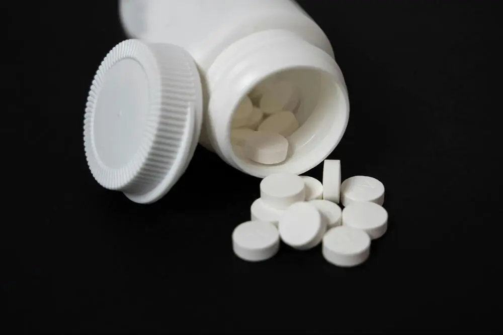 White pills spilling from a bottle against a black background